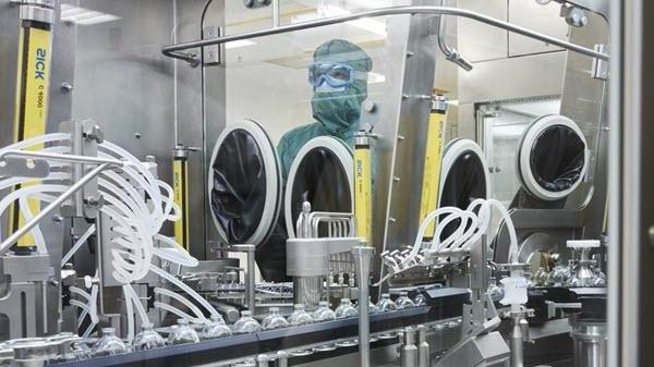 A manufacturing employee in a mask and gown looks over a bottling line